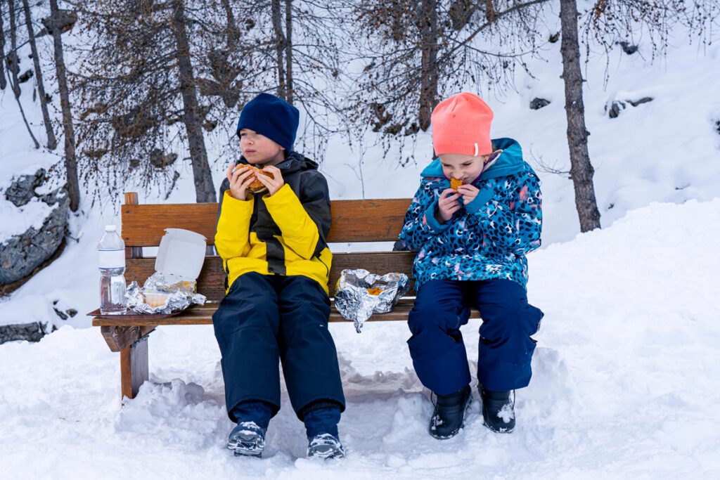 Two kids enjoy snacks while skiing