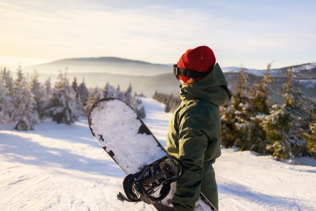 A snowboarder stands at a snowy mountain summit