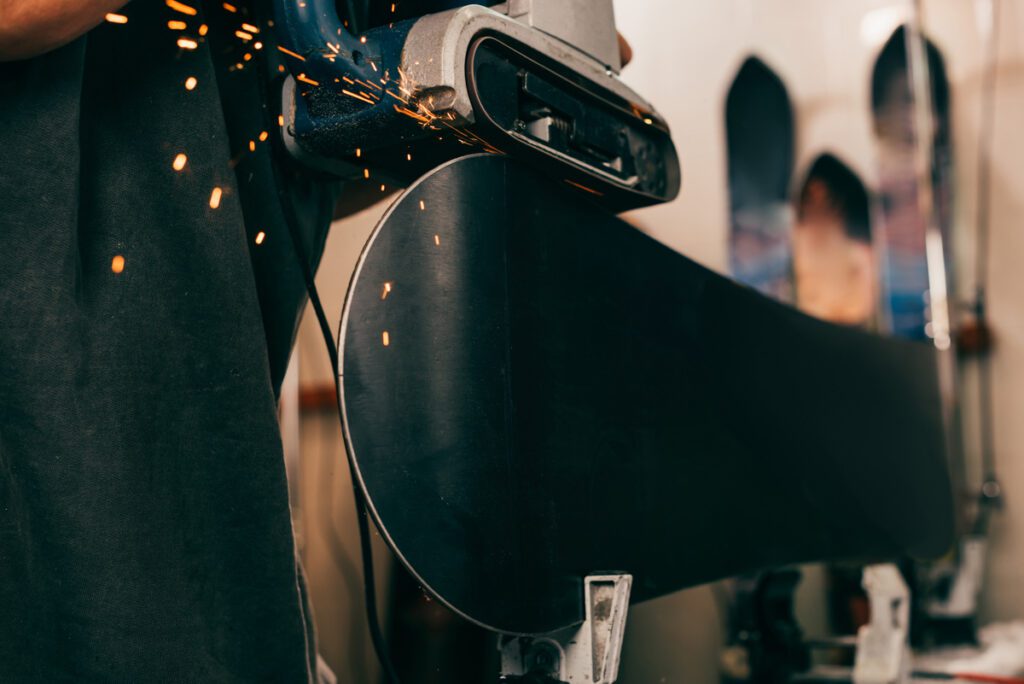 A machine sharpens the edges on a snowboard for summer storage